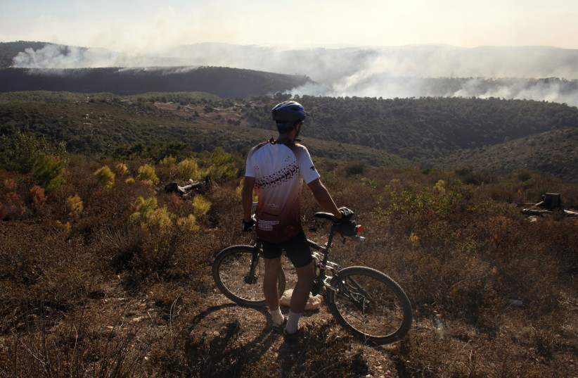A man stands next to his bicycle as he looks at a forest fire on Mount Carmel, near the northern city of Haifa December 3, 2010. International firefighting teams were on Friday helping Israel battle a huge forest fire close to the port city of Haifa that has killed at least 42 people and forced mass (credit: REUTERS/NIR ELIAS)