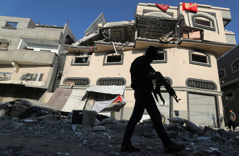 A Palestinian militant walks past the home of Islamic Jihad field commander Baha Abu Al-Atta after it was hit by an Israeli strike that killed him in Gaza City (photo credit: REUTERS/MOHAMMED SALEM)