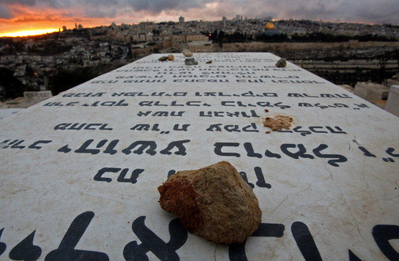 Stones placed in remembrance lie on grave tablets on the Mount of Olives Jewish cemetary as the sun sets in Jerusalem (credit: LASZLO BALOGH/ REUTERS)