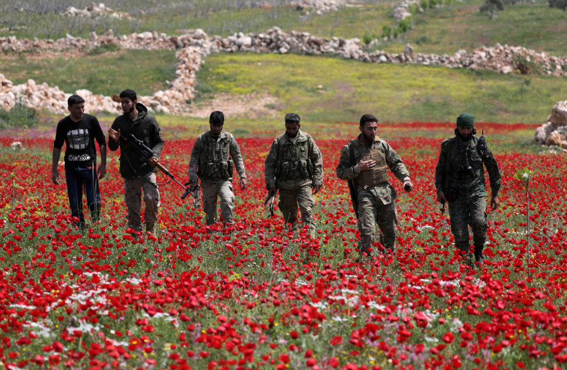 TURKEY-BACKED Syrian rebel fighters walk through a field of flowers in Idlib’s southern countryside, in Syria in April (credit: KHALIL ASHAWI / REUTERS)
