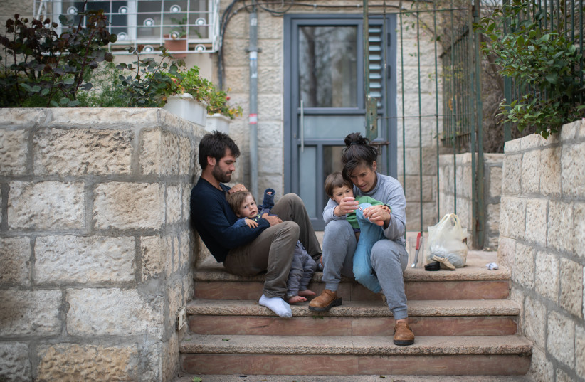 An Israeli family sits on the steps outside their apartment building in Jerusalem, as they stay at home with their children during a nation-wide quarantine, on March 31, 2020.  (credit: HADAS PARUSH/FLASH90)