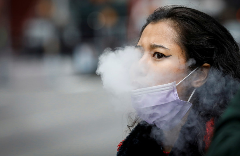 A woman exhales after vaping in Times Square, during the coronavirus disease (COVID-19) outbreak, in New York City, U.S., March 31, 2020 (photo credit: REUTERS/BRENDAN MCDERMID)