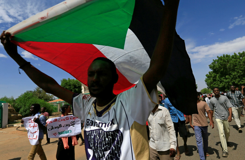 A Sudanese protester carries their national flag as they march in a demonstration to mark the anniversary of a transitional power-sharing deal with demands for quicker political reforms in Khartoum, Sudan August 17, 2020 (credit: REUTERS/MOHAMED NURELDIN ABDALLAH)