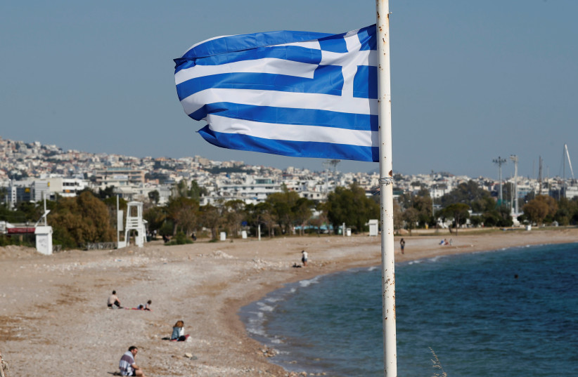 A Greek national flag flutters as people visit a beach, following the coronavirus disease (COVID-19) outbreak, in Athens, Greece, April 28, 2020. (photo credit: GORAN TOMASEVIC/REUTERS)