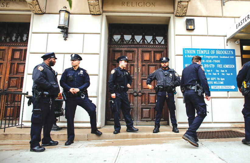 New York police officers stand guard at the door of the Union Temple of Brooklyn, in 2018. (credit: KENA BETANCUR/AFP/GETTY IMAGES/JTA)