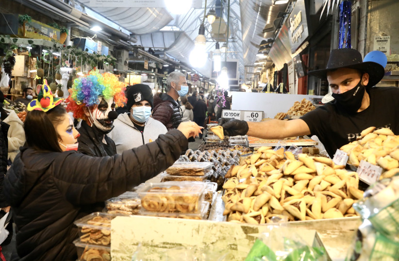 Israelis in Purim costume buy hamentashen from a Mahaneh Yehuda seller. (credit: MARC ISRAEL SELLEM/THE JERUSALEM POST)