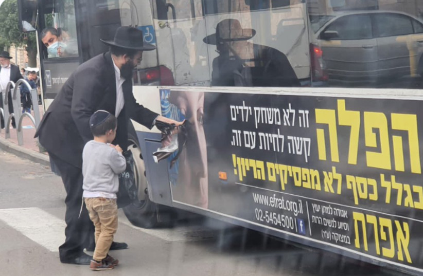 A father shows his son how to pull a woman's face off an anti-abortion organization's bus ad (credit: ISRAEL COHEN ON TWITTER)