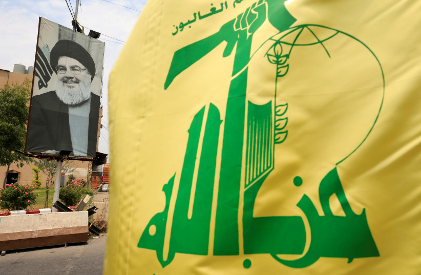A Hezbollah flag and a poster depicting Lebanon's Hezbollah leader Sayyed Hassan Nasrallah are pictured along a street, near Sidon, Lebanon July 7, 2020 (credit: REUTERS/ALI HASHISHO)
