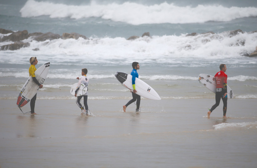 SURFERS CARRY their boards before entering the water in Netanya.  (credit: BAZ RATNER/REUTERS)
