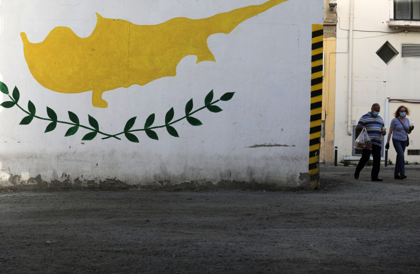  People wearing protective masks walk next to a Cypriot flag painted on a wall in capital Nicosia, Cyprus (credit: YIANNIS KOURTOGLOU/REUTERS)