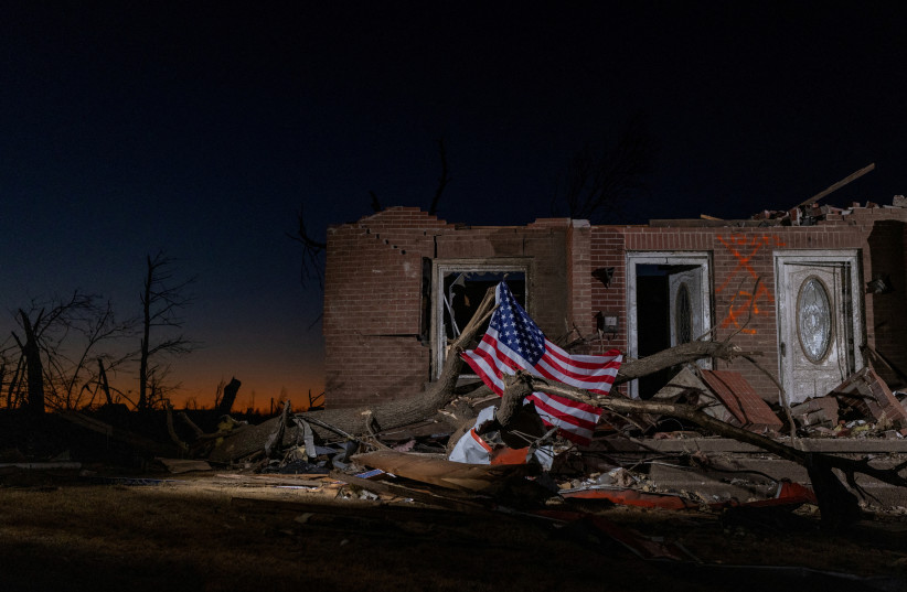 A US flag is tied to a fallen tree in front of a destroyed residence in the aftermath of a tornado in Mayfield, Kentucky, US, December 13, 2021. (photo credit: REUTERS/ADREES LATIF)