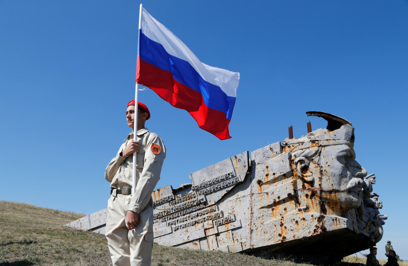 An activist holds Russia's national flag, during a rally at the war memorial complex Savur-Mohyla, damaged in the recent fighting with Ukraine's government forces,marking the 78th anniversary of the liberation of the Donbas region,Ukraine September 8, 2021. (credit: REUTERS/ALEXANDER ERMOCHENKO)