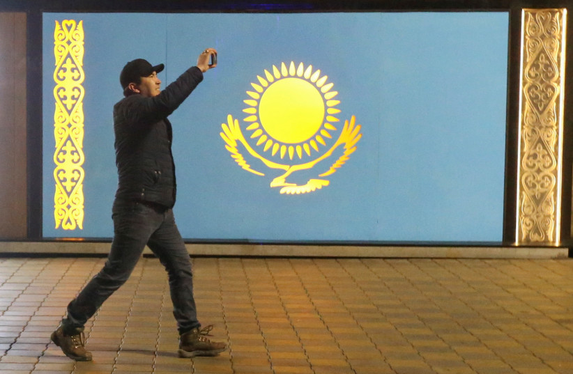  A man holds a mobile phone while walking past a board with a Kazakh state flag during a protest against LPG cost rise following authorities' decision to lift price caps on liquefied petroleum gas in Almaty, Kazakhstan January 5, 2022 (credit: REUTERS/PAVEL MIKHEYEV)