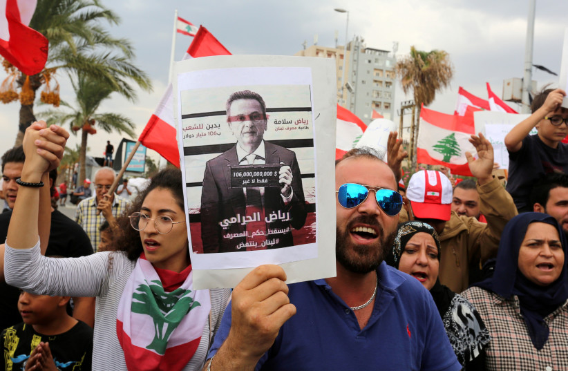 Demonstrators carry Lebanese flags and a banner depicting Lebanon's Central Bank Governor Riad Salameh, as they head towards the central bank building during an anti-government protest in the southern city of Tyre, Lebanon October 23, 2019 (credit: AZIZ TAHER/REUTERS)