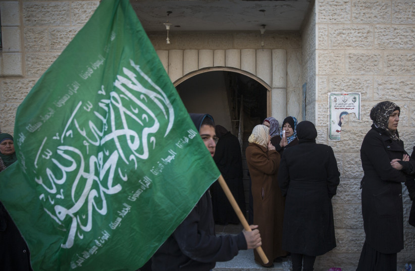  A young boy carrying a Hamas flag walks past Palestinian women gathered as they wait for the funeral of a young Palestinian girl, outside the family's home in the Qalandiya Refugee camp in the West Bank, on December 18, 2015.  (credit: HADAS PARUSH/FLASH90)