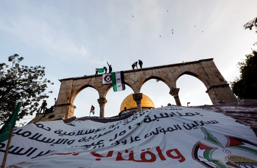  Palestinians hang a giant banner during Eid al-Fitr prayers which marks the end of the holy fasting month of Ramadan, on the compound known to Muslims as Noble Sanctuary and to Jews as Temple Mount in Jerusalem's Old City May 2, 2022. (credit: REUTERS/AMMAR AWAD)