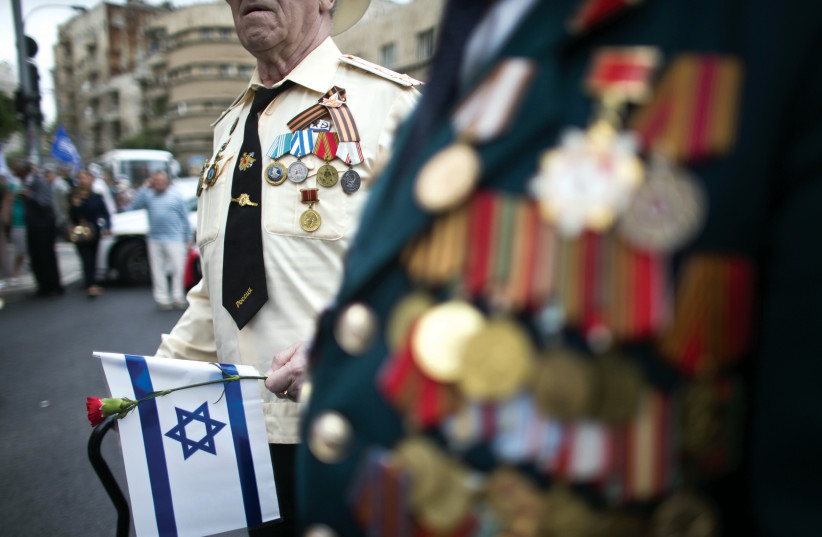  A World War II veteran holds a flower and Israel’s national flag during a march in Jerusalem commemorating the 70th anniversary of VE (Victory in Europe) Day on May 10, 2015. (credit: RONEN ZVULUN/REUTERS)