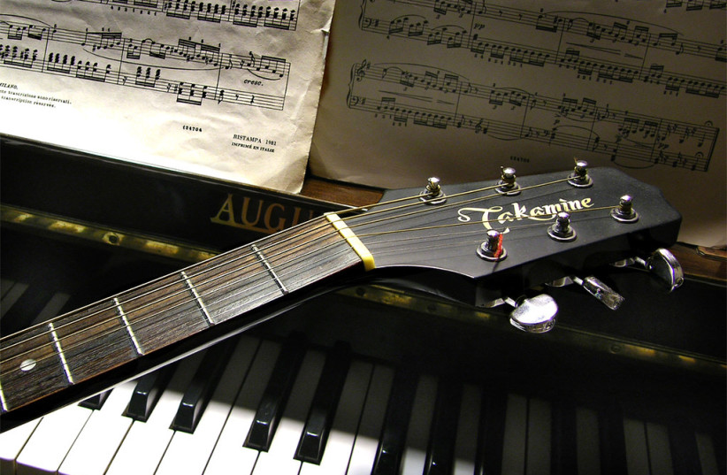  A guitar lies across a piano. (photo credit: FLICKR)