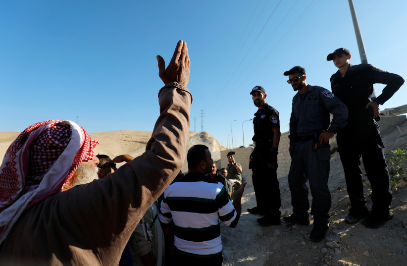  A Palestinian man gestures as Israeli policemen stand guard in the Bedouin village of Khan al-Ahmar that Israel plans to demolish, in the West Bank October 16, 2018. (photo credit: REUTERS/MOHAMAD TOROKMAN)