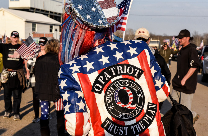  A woman wears a jacket with a QAnon logo while hundreds of vehicles including 18-wheeler trucks, RVs and other cars are parked as part of a rally at Hagerstown Speedway after some of them arrived as part of a convoy that traveled across the country headed to Washington D.C. to protest coronavirus d (credit: REUTERS/STEPHANIE KEITH)