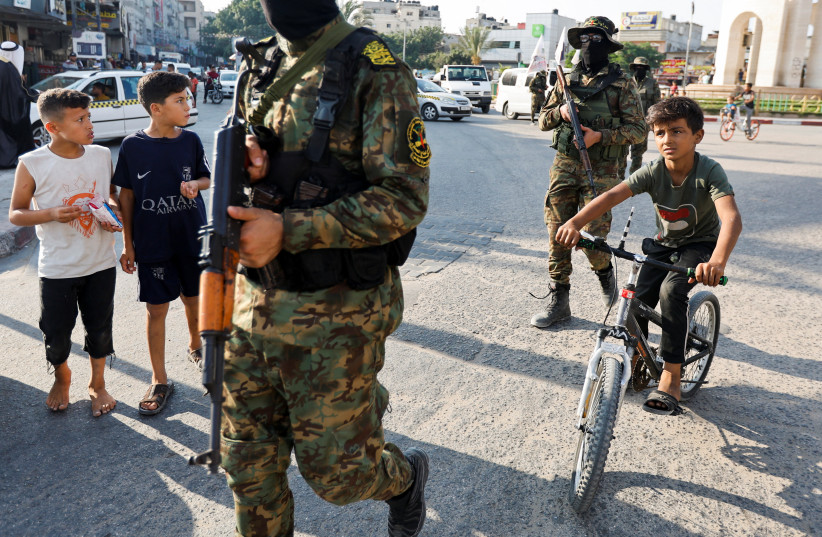  PALESTINIAN CHILDREN are nearby as Islamic Jihad militants march in Rafah, Gaza Strip, on Wednesday. To many Arabs, Gaza militants are one of the groups that take civilians as human shields to serve Iran’s grand expansionist strategy, says the writer.  (credit: IBRAHEEM ABU MUSTAFA/REUTERS)