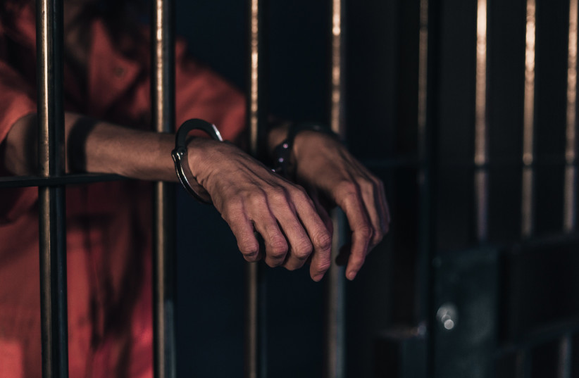  Handcuffed hands rest on prison bars. (Illustrative) (photo credit: MATTHEW HENRY)