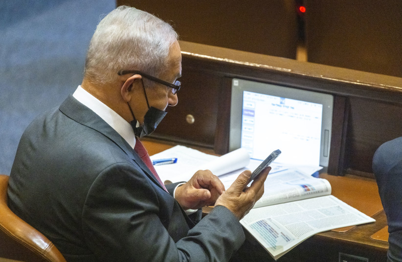  Benjamin Netanyahu checking his phone at the Knesset plenum, October 27, 2021 (credit: OLIVIER FITOUSSI/FLASH90)