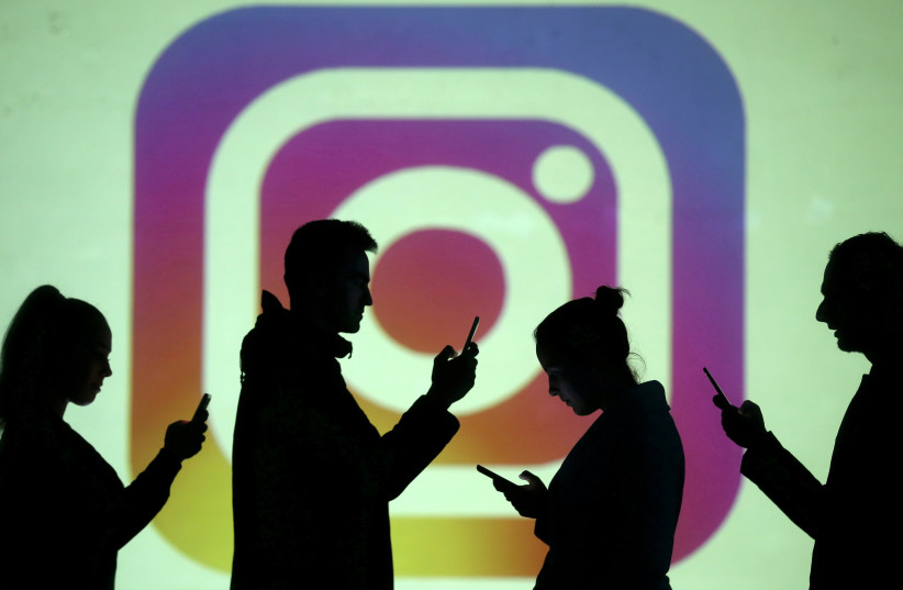 Silhouettes of mobile users are seen next to a screen projection of Instagram logo in this picture illustration taken March 28, 2018. (credit: REUTERS/DADO RUVIC/ILLUSTRATION/FILE PHOTO)