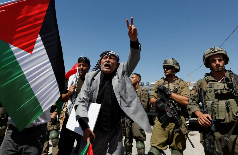 Palestinian protester gestures as IDF soldiers stand guard during a demonstration against Israeli settlements, in Masafer Yatta near Hebron in the West Bank, September 17, 2022.