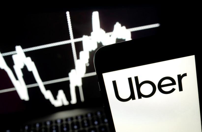 Logo of Uber is seen on a smartphone screen as a picture of stock exchange graph is displayed on a computer screen in this illustration picture, May 7, 2019. (credit: REUTERS/KACPER PEMPEL/ILLUSTRATION)
