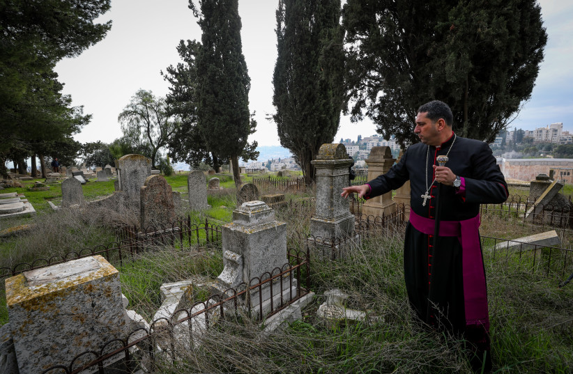 A priest shows a gravestone allegedly vandalized by Jewish men in the Christian cemetery on Mount Zion, in the Old City of Jerusalem, January 4, 2023. (credit: JAMAL AWAD/FLASH90)