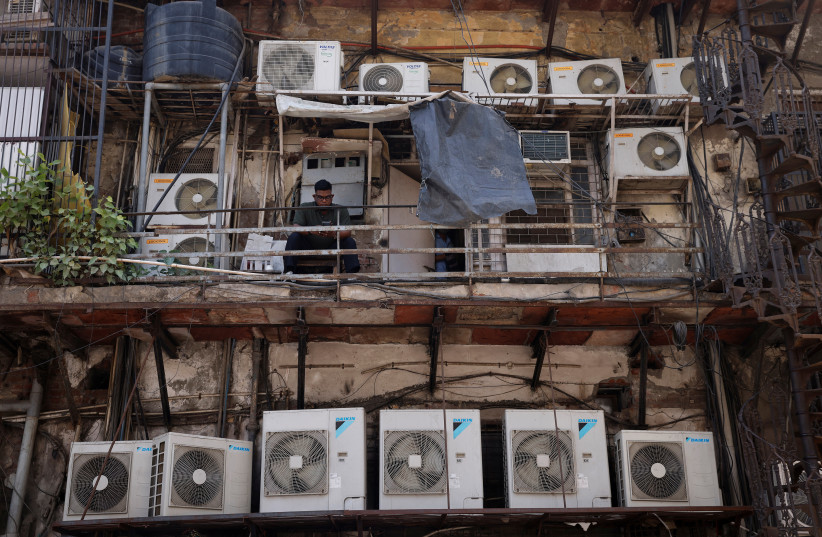  A man uses his mobile phone as he sits amidst the outer units of air conditioners, at the rear of a commercial building in New Delhi, India, April 30, 2022 (credit: ADNAN ABIDI/ REUTERS)