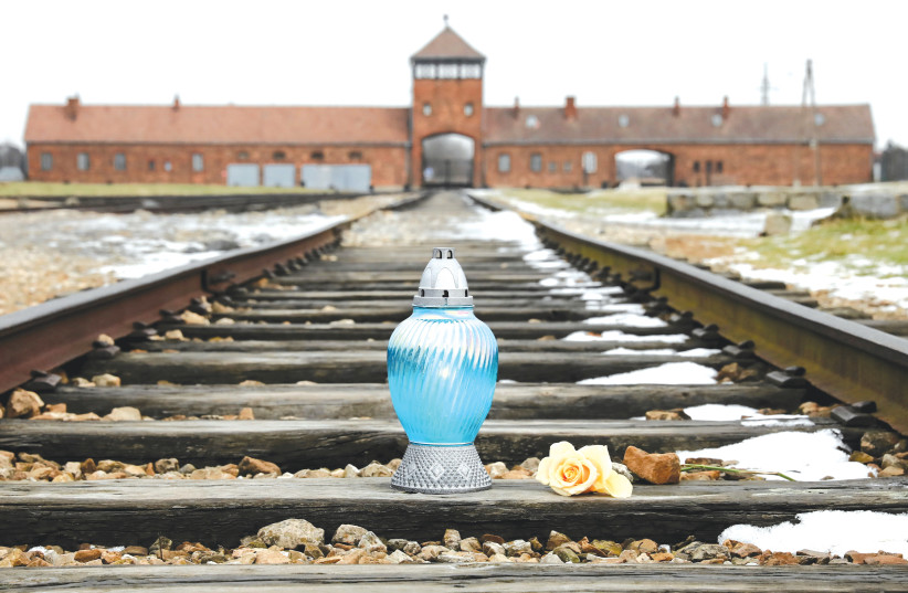  A CANDLE is lit and a flower is placed on the railway tracks at Birkenau, on International Holocaust Remembrance Day, last year. (photo credit: Agencja Wyborcza.pl/Reuters)
