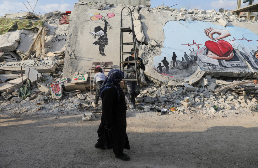  A woman walks past street art on the rubble of damaged buildings in the rebel-held town of Jandaris, in the aftermath of a deadly earthquake, in Syria February 22, 2023 (credit: REUTERS/KHALIL ASHAWI)