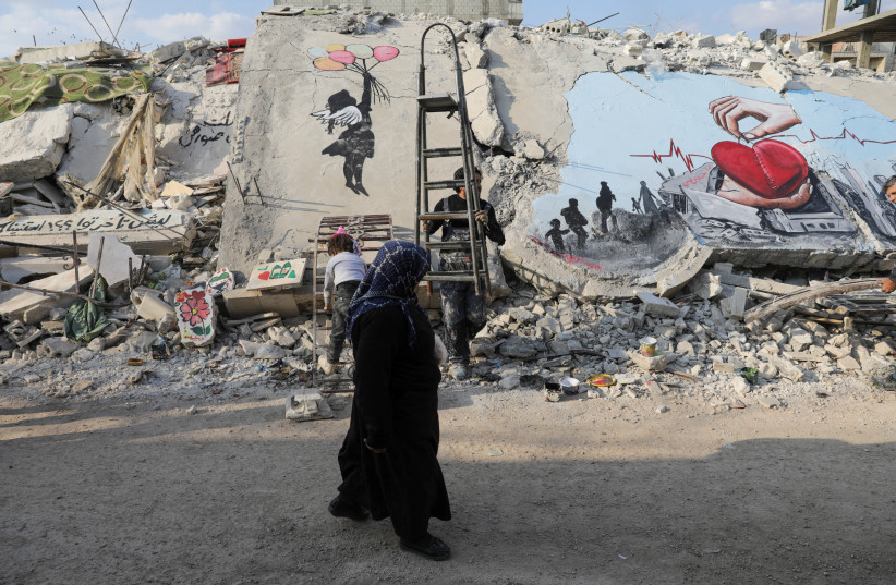 A woman walks past street art on the rubble of damaged buildings in the rebel-held town of Jandaris, in the aftermath of a deadly earthquake, in Syria February 22, 2023