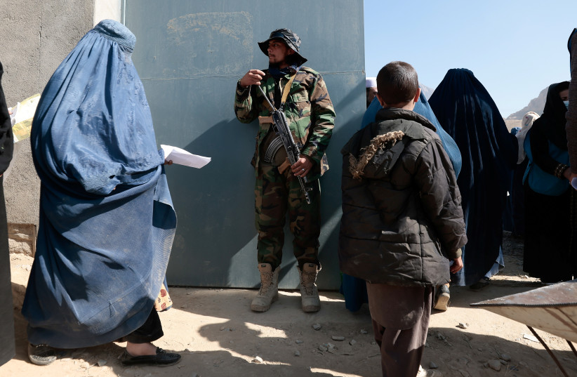 A Taliban fighter stands on guard as displaced Afghan women walk into an UNHCR distribution center to receive aid supply on the outskirts of Kabul, Afghanistan, October 28, 2021. (photo credit: REUTERS/ZOHRA BENSEMRA)