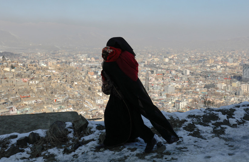 An Afghan woman holds her child as she walks on a snow-covered street on the TV mountain in Kabul, Afghanistan, January 25, 2023. (photo credit:  REUTERS/ALI KHARA)