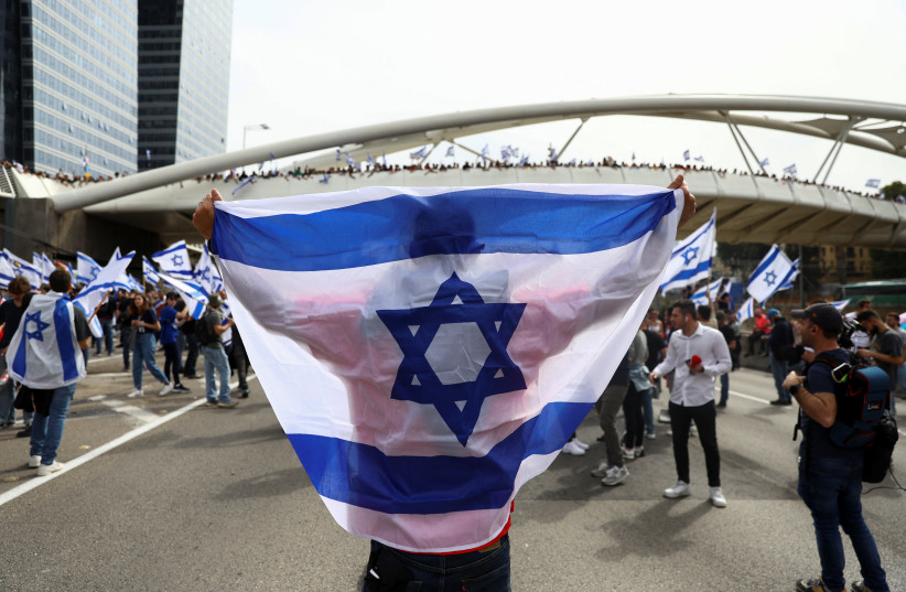  A demonstrator holds an Israeli flag as they attend the "Day of Paralysis" protest, as Israeli Prime Minister Benjamin Netanyahu's nationalist coalition government presses on with its judicial overhaul, in Tel Aviv, Israel March 23, 2023.  (photo credit: RONEN ZVULUN/REUTERS)