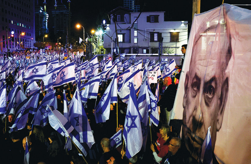  PEOPLE HOLD Israeli flags next to a banner of Prime Minister Benjamin Netanyahu during a demonstration in Tel Aviv last week against the judicial overhaul. (photo credit: RONEN ZVULUN/REUTERS)