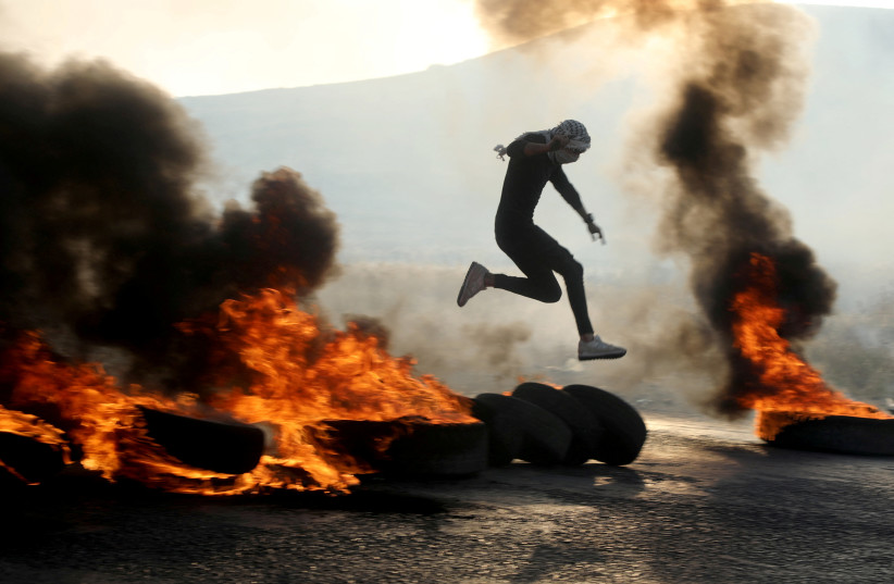  Palestinian man jumps over burning tires as people protest over tensions in Jerusalem's Al-Aqsa Mosque, at Huwara checkpoint, near Nablus in the Israeli-occupied West Bank May 29, 2022 (photo credit: REUTERS)