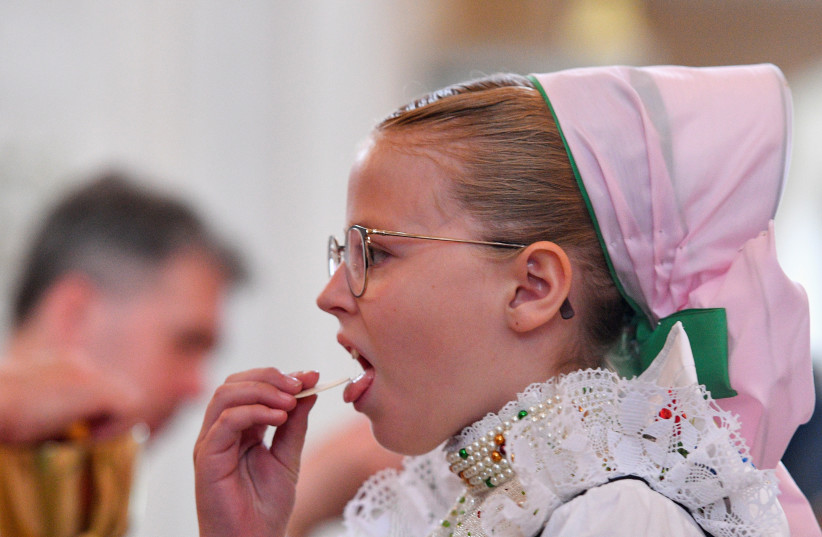  ACCUSED OF ‘desecrating the host’: A girl in traditional clothing takes sacramental bread in Germany, 2022.  (photo credit: Matthias Rietschel/Reuters)