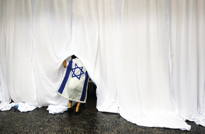  A BOY covered in an Israeli flag lifts a curtain during a welcoming ceremony at Ben-Gurion Airport for new immigrants from North America.  (photo credit: BAZ RATNER/REUTERS)