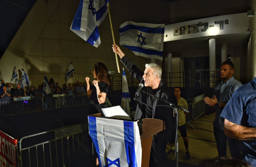  Opposition Leader Yair Lapid hold an Israeli flag up high at a judicial reform protest in Hod HaSharon on April 22, 2023. (credit: ELAD GUTMAN)