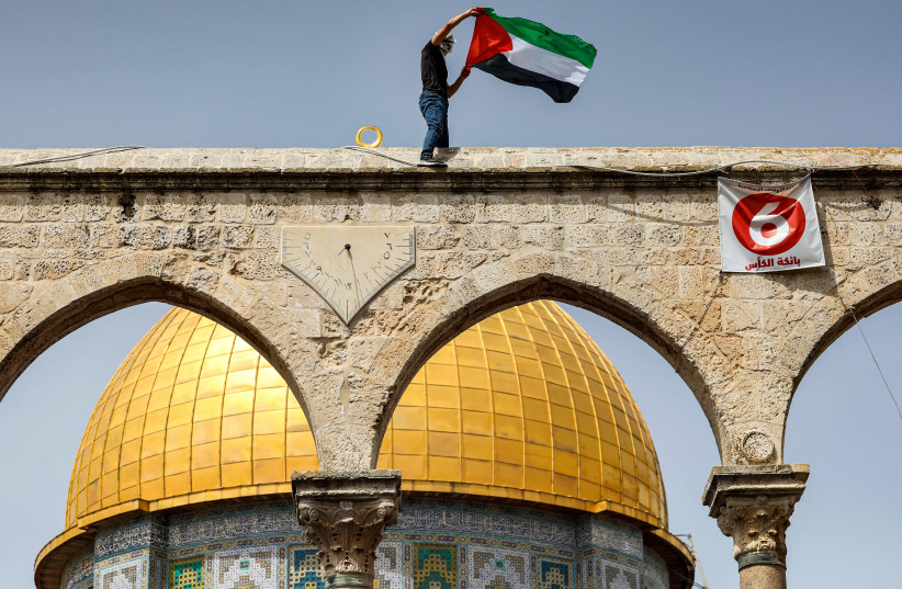  A man waves a Palestinian flag while standing above a sundial along a colonnade before the Dome of the Rock shrine at al-Aqsa mosque compound in the Old City of Jerusalem on April 7, 2023 on the third Friday Noon prayer during the Muslim holy fasting month of Ramadan.  (photo credit:  AHMAD GHARABLI/AFP VIA GETTY IMAGES)