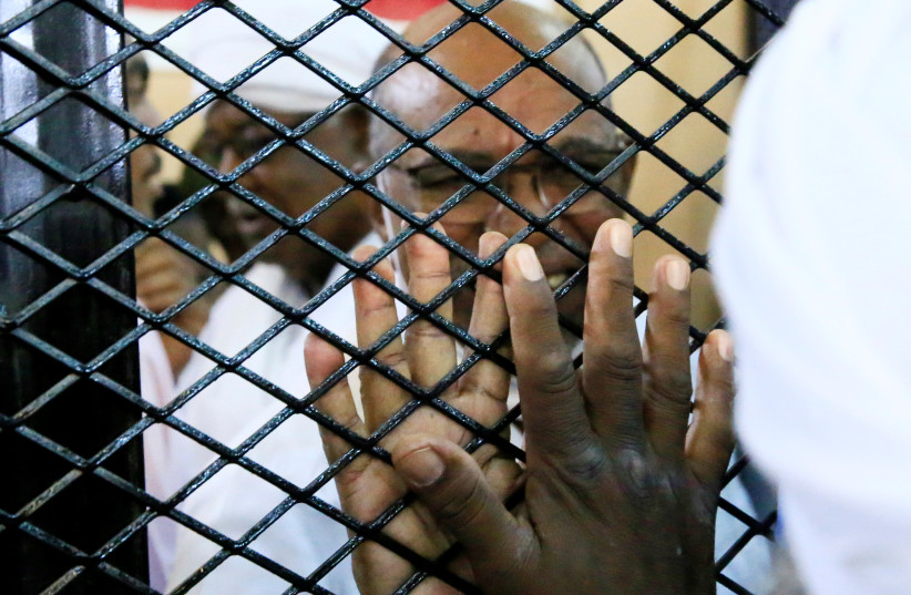  Sudan's ousted President Omar al-Bashir greets a supporter from inside the defendant's cage during his and some of his former allies trial over the 1989 military coup that brought the autocrat to power in 1989, at a courthouse in Khartoum, Sudan September 15, 2020 (photo credit: MOHAMED NURELDIN ABDALLAH/REUTERS)