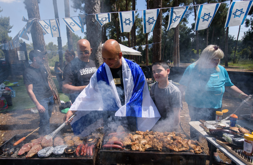  A man wrapped in an Israeli flag tends to a barbecue at an Independence Day celebration, April 26, 2023. (credit: AYAL MARGOLIN/FLASH90)