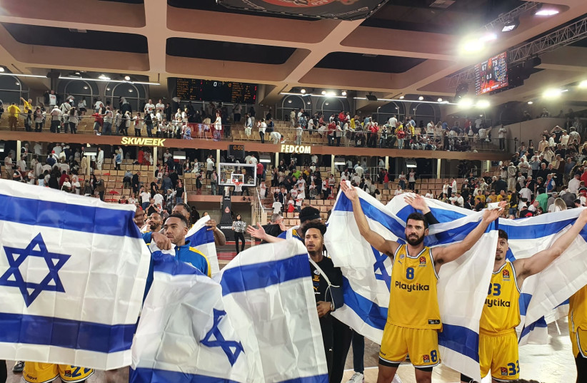 MACCABI TEL AVIV players and fans celebrate with Israeli flags at the Gaston Medecin Arena after the yellow-and-blue beat host AS Monaco 79-67 on Tuesday night in Game 1 of their Euroleague quarterfinal series. (photo credit: MACCABI TEL AVIV/COURTESY)