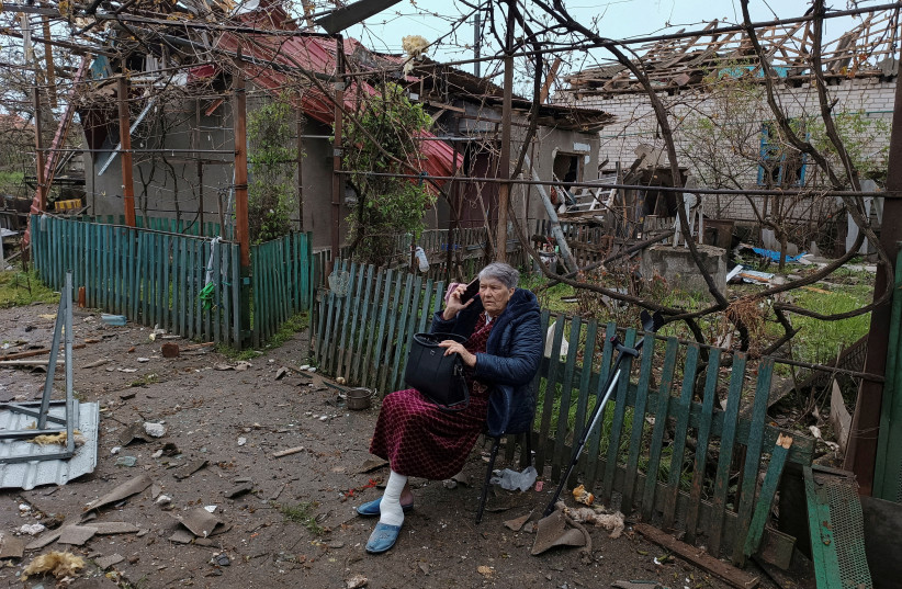 A local woman speaks on her phone as she sits on a bench next to a residential house damaged by a Russian missile strike, amid Russia's attack on Ukraine, in Mykolaiv, Ukraine April 27, 2023. (credit: REUTERS/Viktoriia Lakezina)