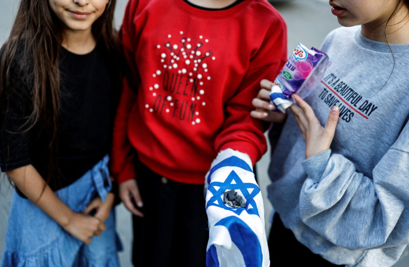  A girl holds up pieces of shrapnel arranged on an Israeli flag after a rocket, launched from Gaza, landed in Sderot, southern Israel, May 2, 2023.  (photo credit: REUTERS/AMIR COHEN)