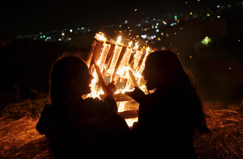 People gather round a bonfire in the Jerusalem neighborhood of Arnona in celebration of the Jewish holiday of Lag Ba'omer, May 8, 2023. (photo credit: MARC ISRAEL SELLEM/THE JERUSALEM POST)